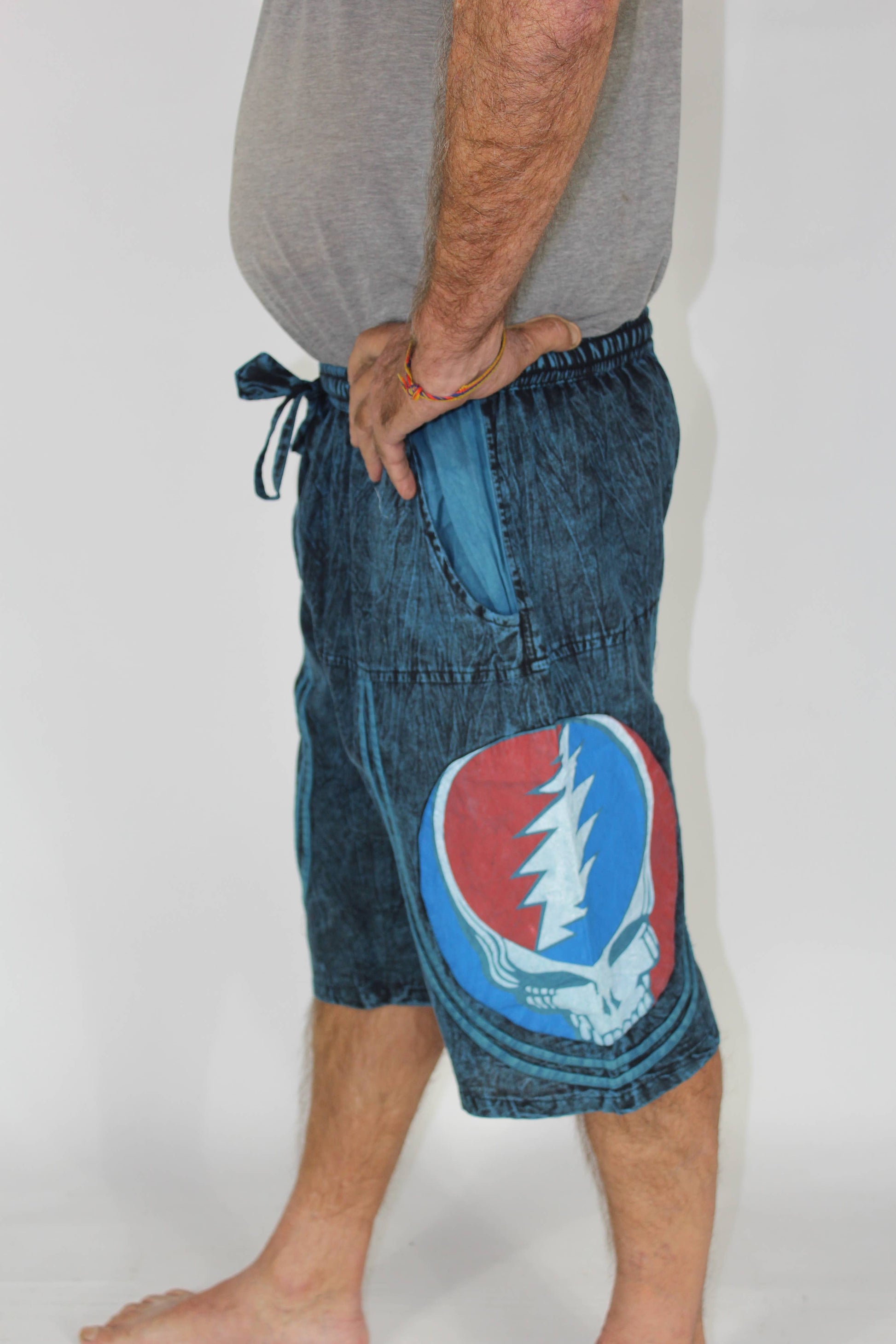 Person wearing blue denim shorts with a Grateful Dead logo on a plain background