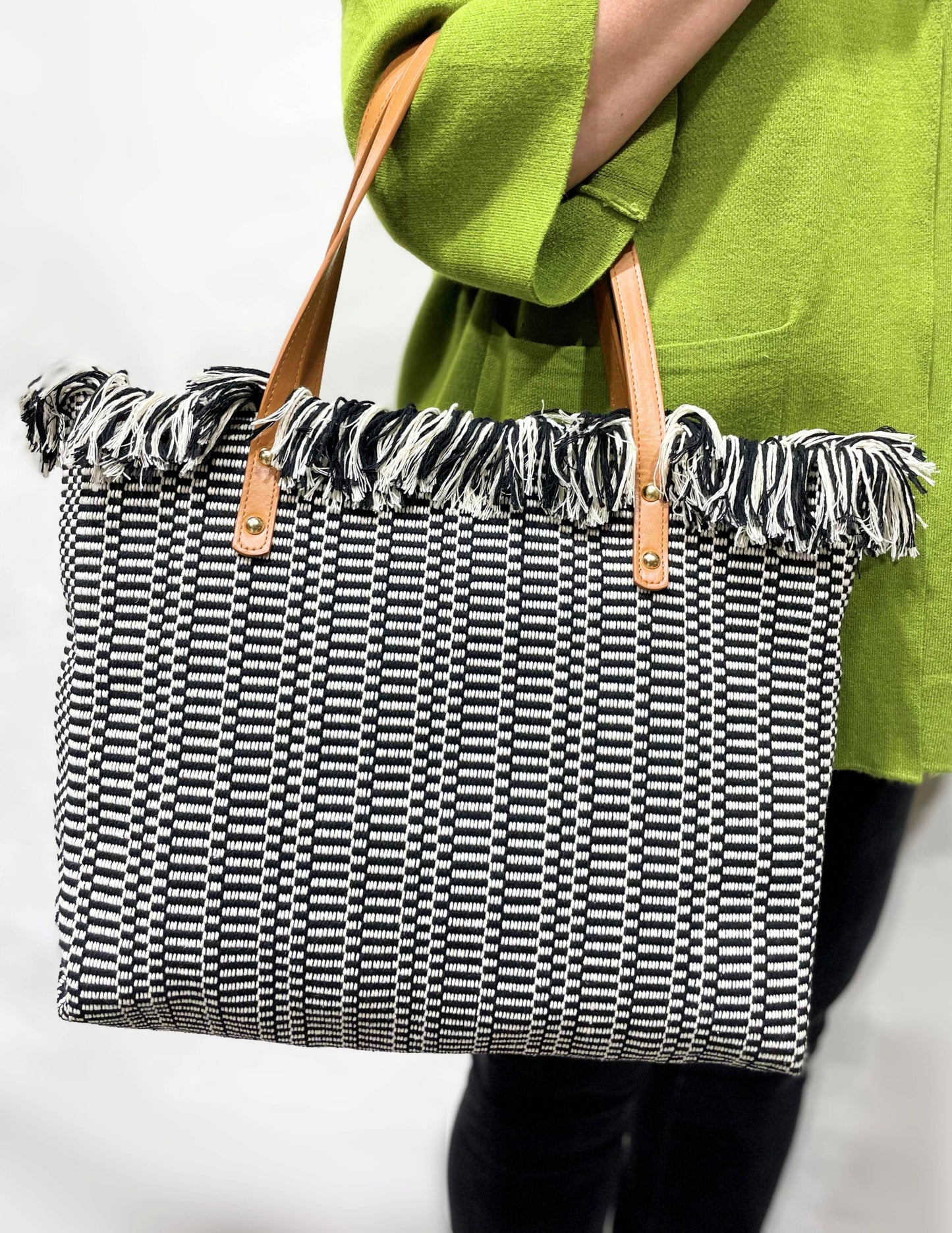 Black and white patterned tote bag with frayed edges held by a person wearing a green coat.