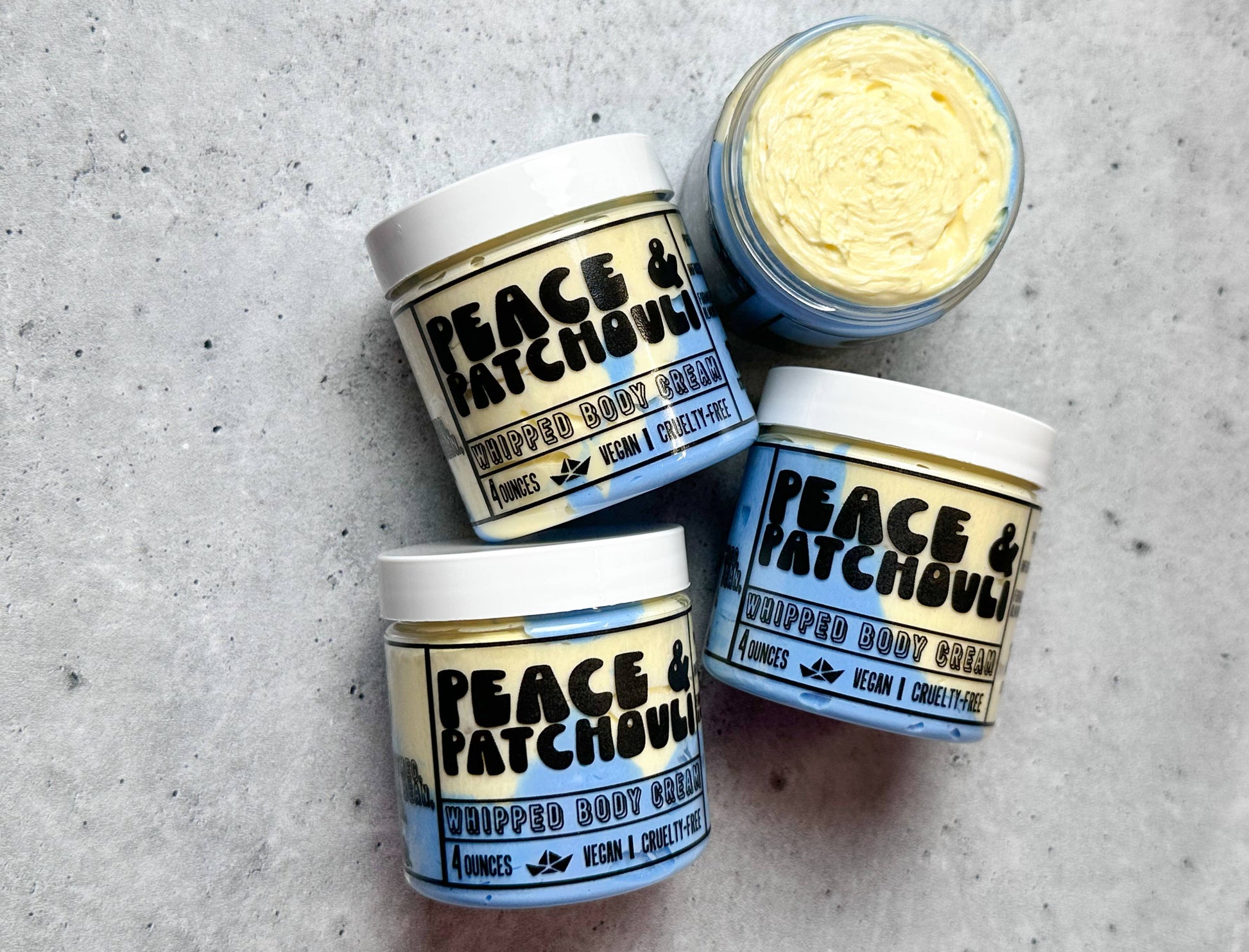 Four jars of 'Peace & Patchouli' whipped body butter on a gray surface.