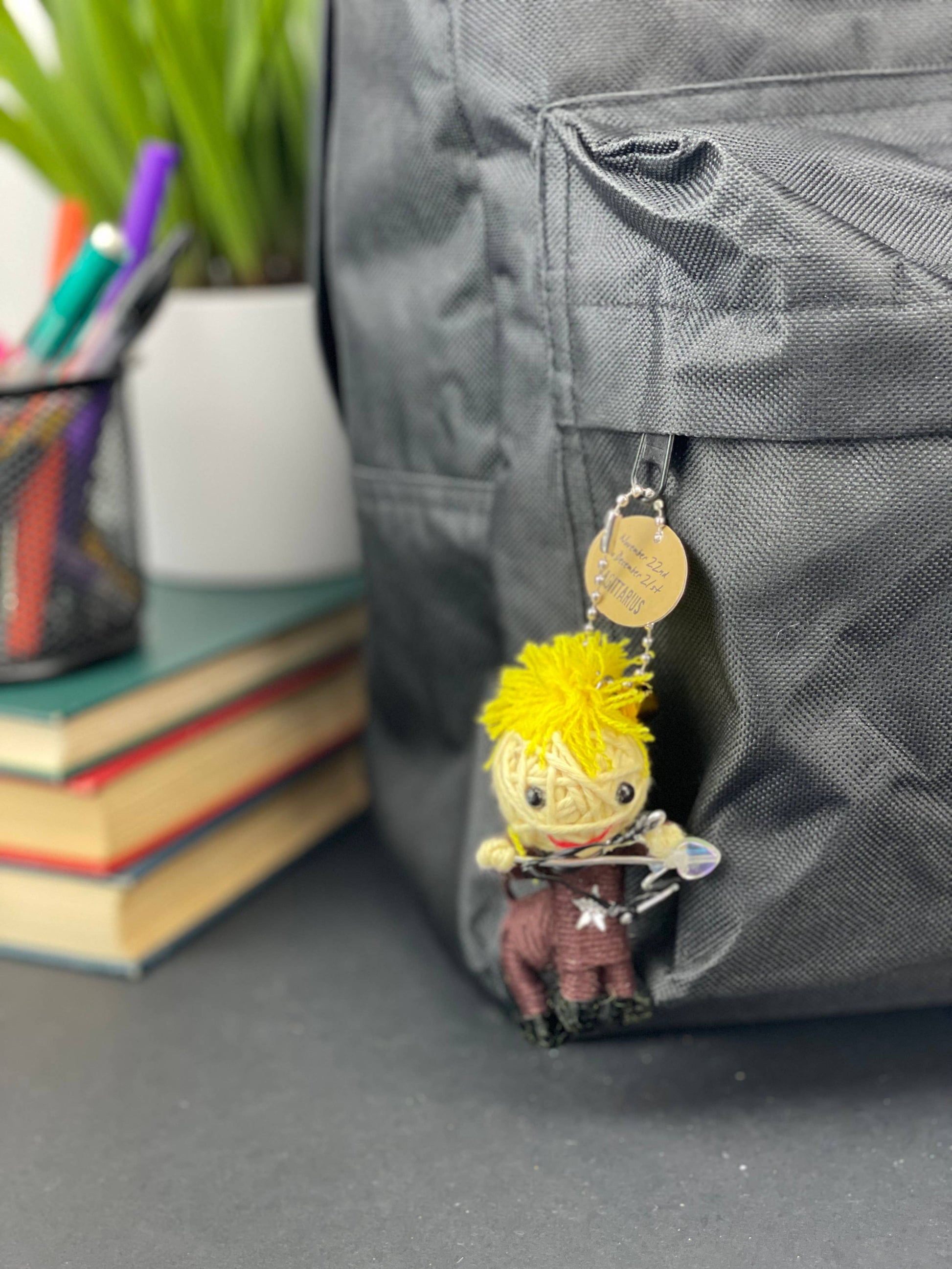 Keychain with character attached to a backpack, with books and stationery items in the background.