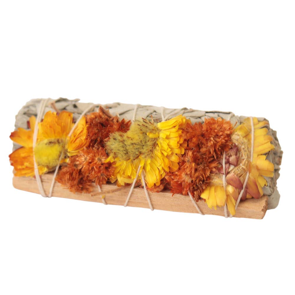 Rolled bundle of dried flowers and herbs on a wooden base with twine, against a white background.