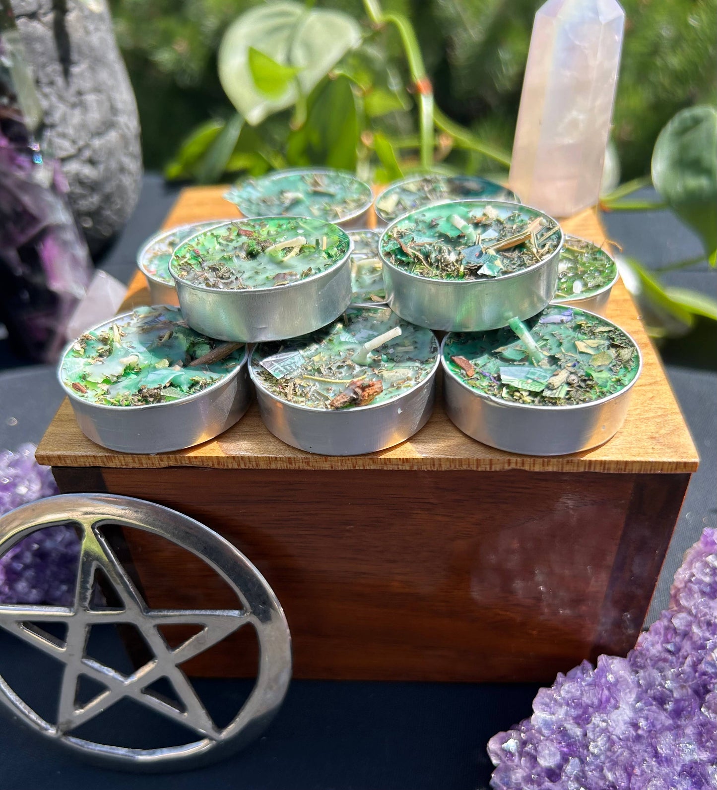 Set of small metal containers with green contents on a wooden stand, surrounded by crystals and plants.
