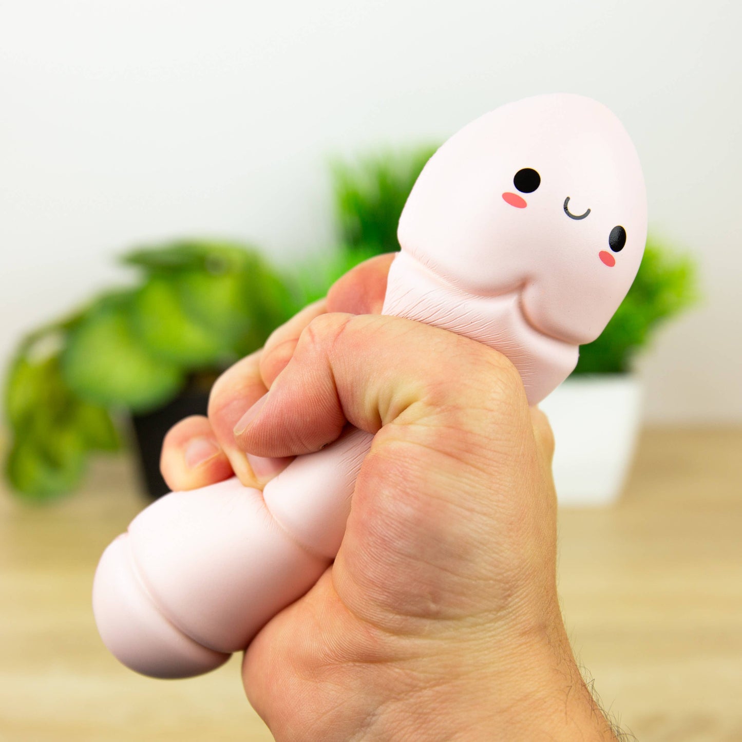 Hand holding a soft, plush toy resembling a worm with a face against a blurred indoor background.