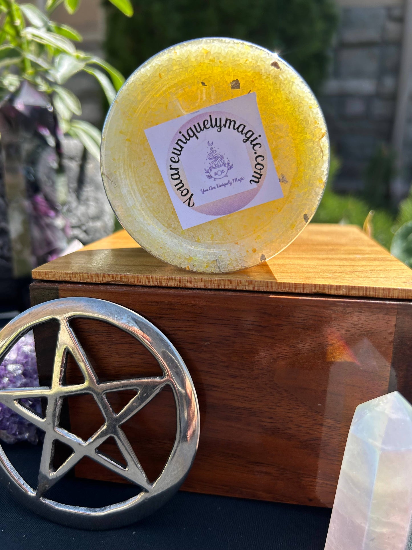 Yellow bath bomb with a brand label on a wooden box, surrounded by crystals and a pentacle symbol.