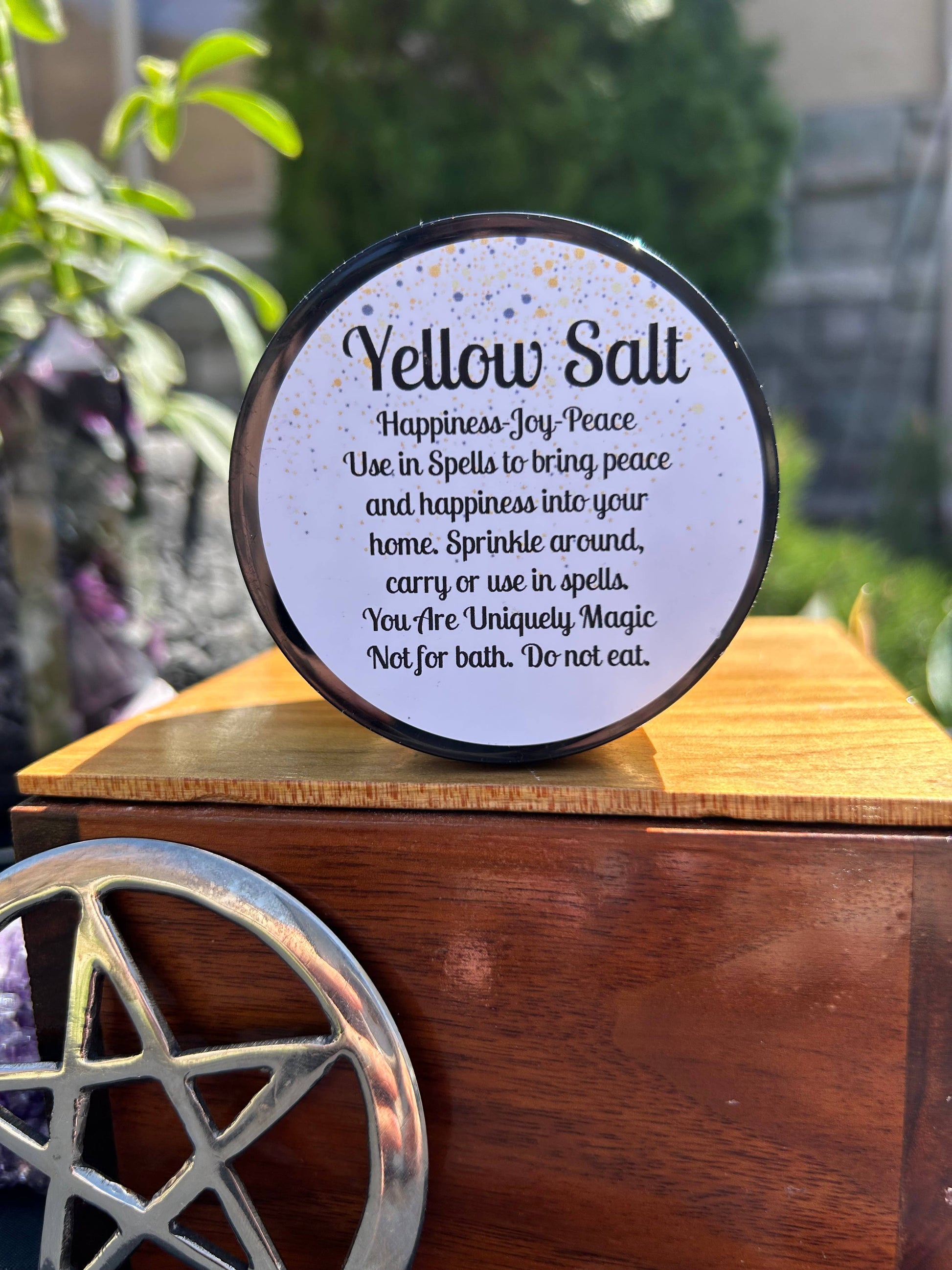 Round container of yellow salt with instructions on a wooden surface with a pentacle symbol.