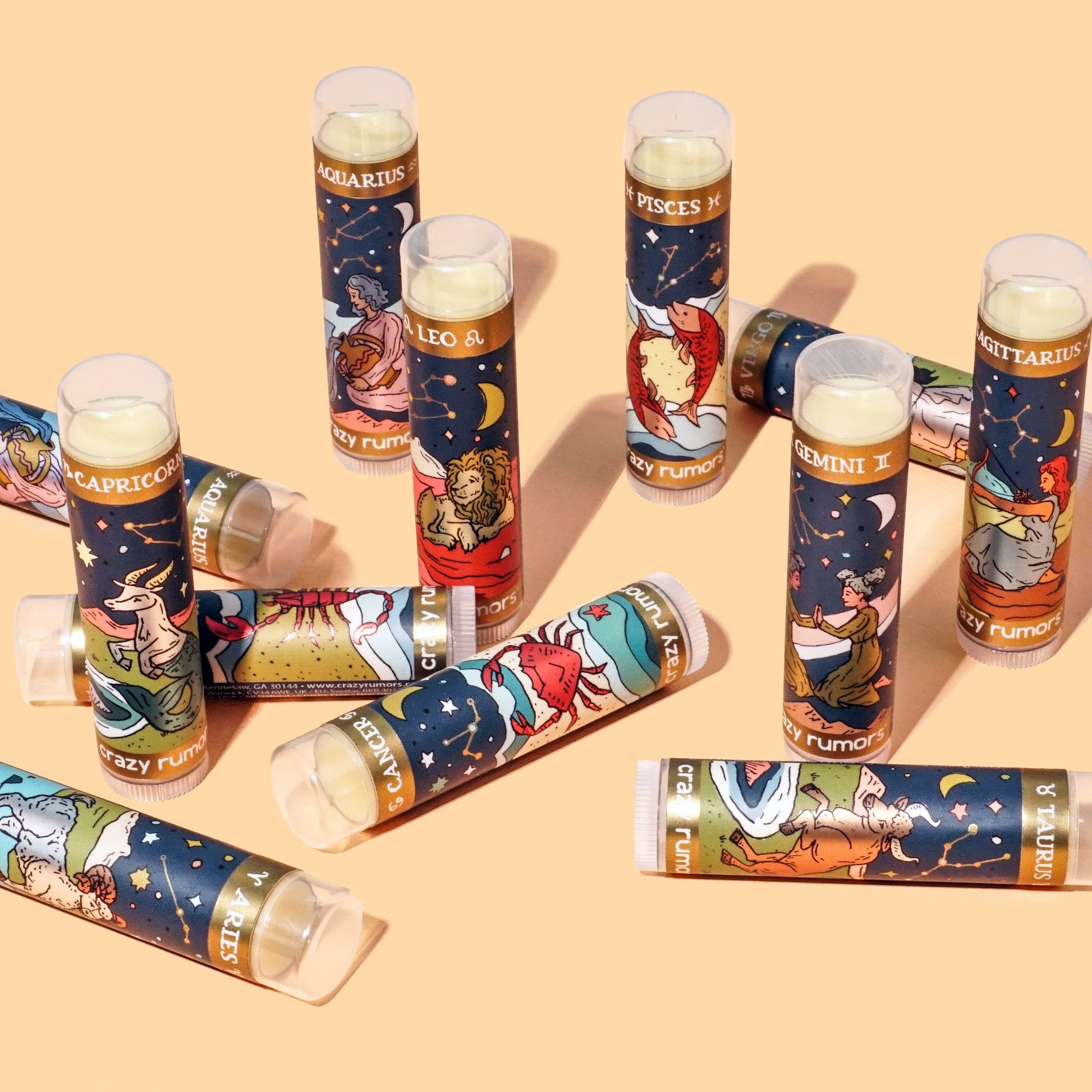 Collection of lip balm tubes with zodiac designs on a beige background