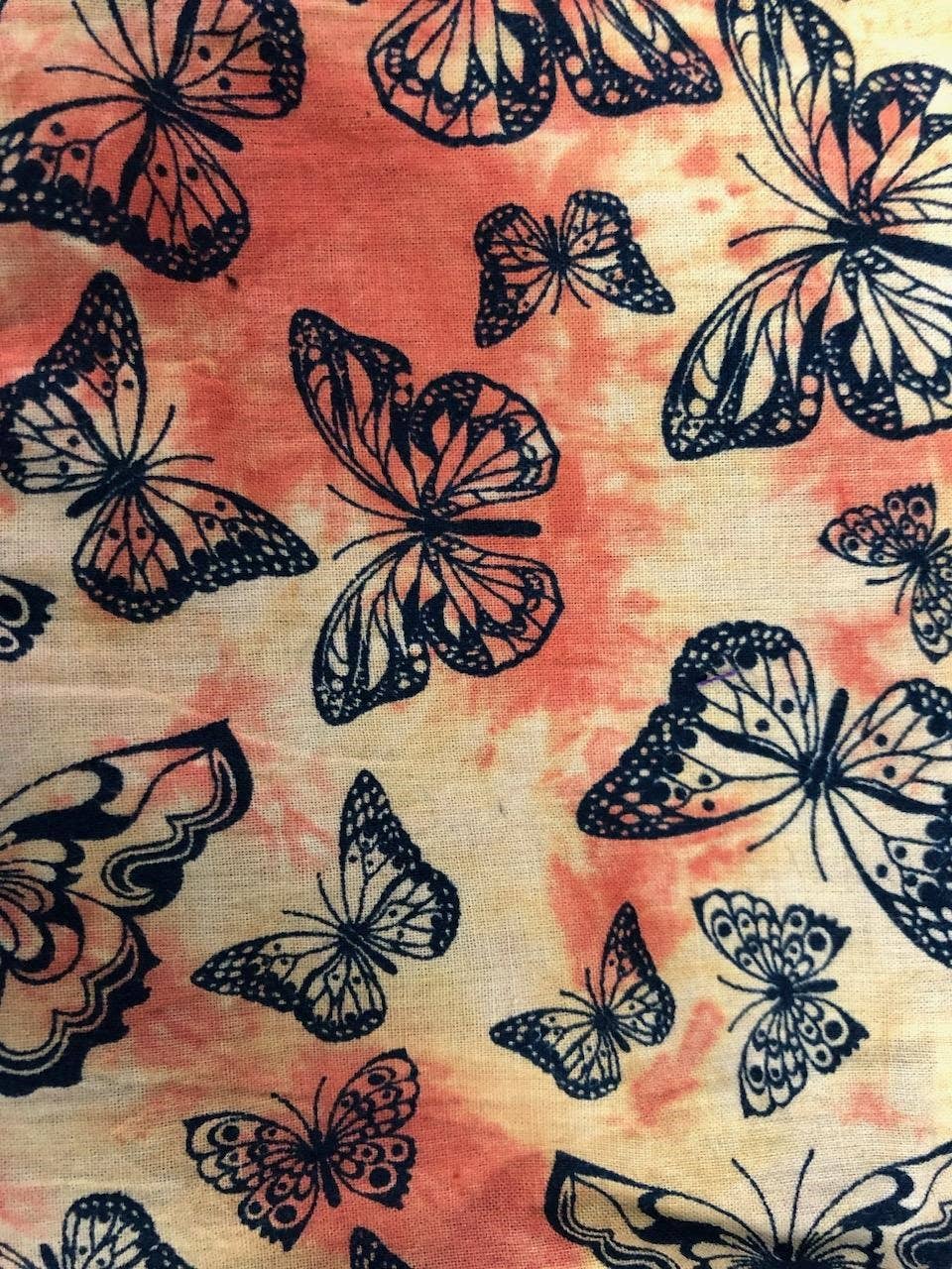 Pattern of black butterflies on a tie-dye background with pink and orange hues